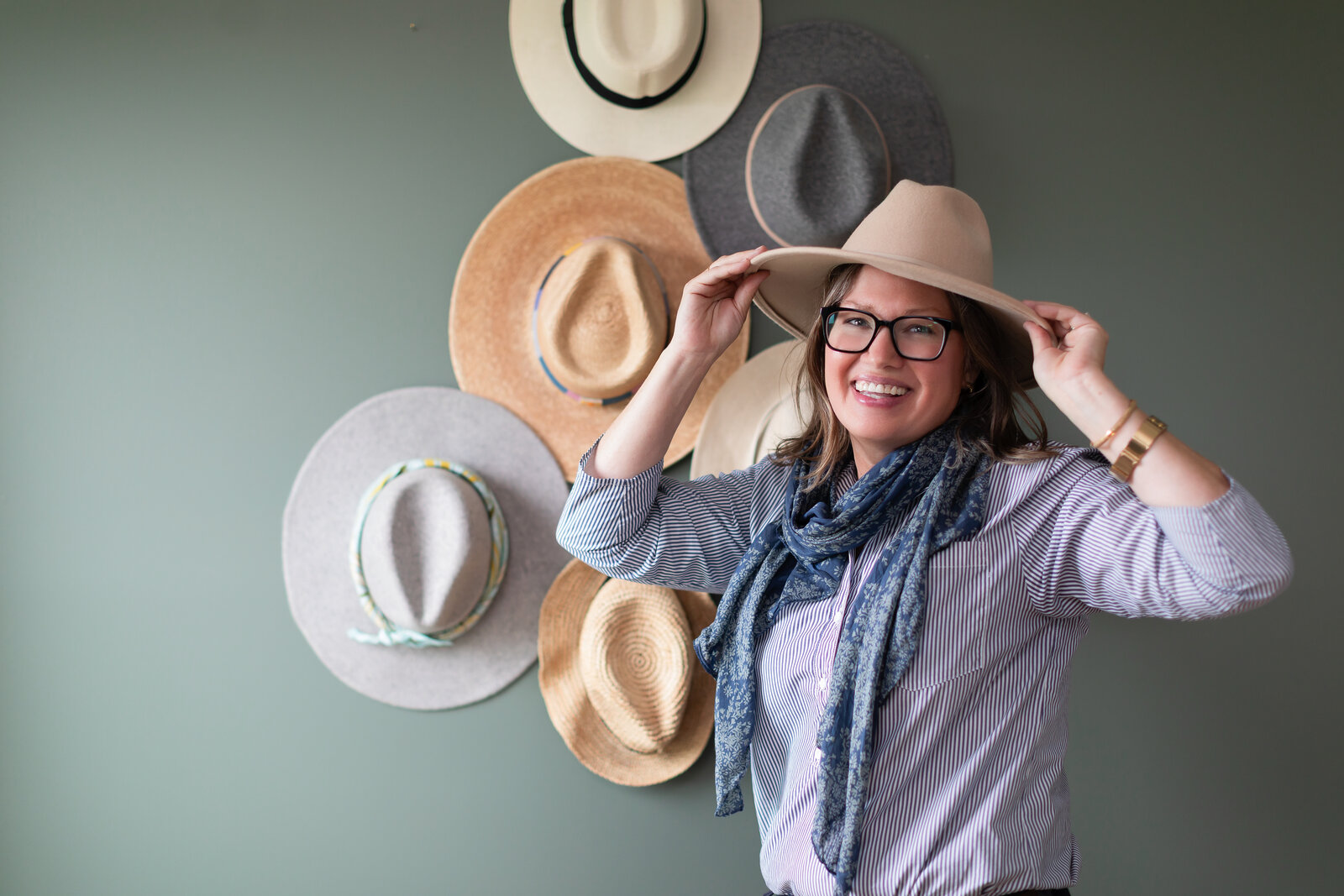 Kelly laughing while trying on hats in front of a wall of hats.