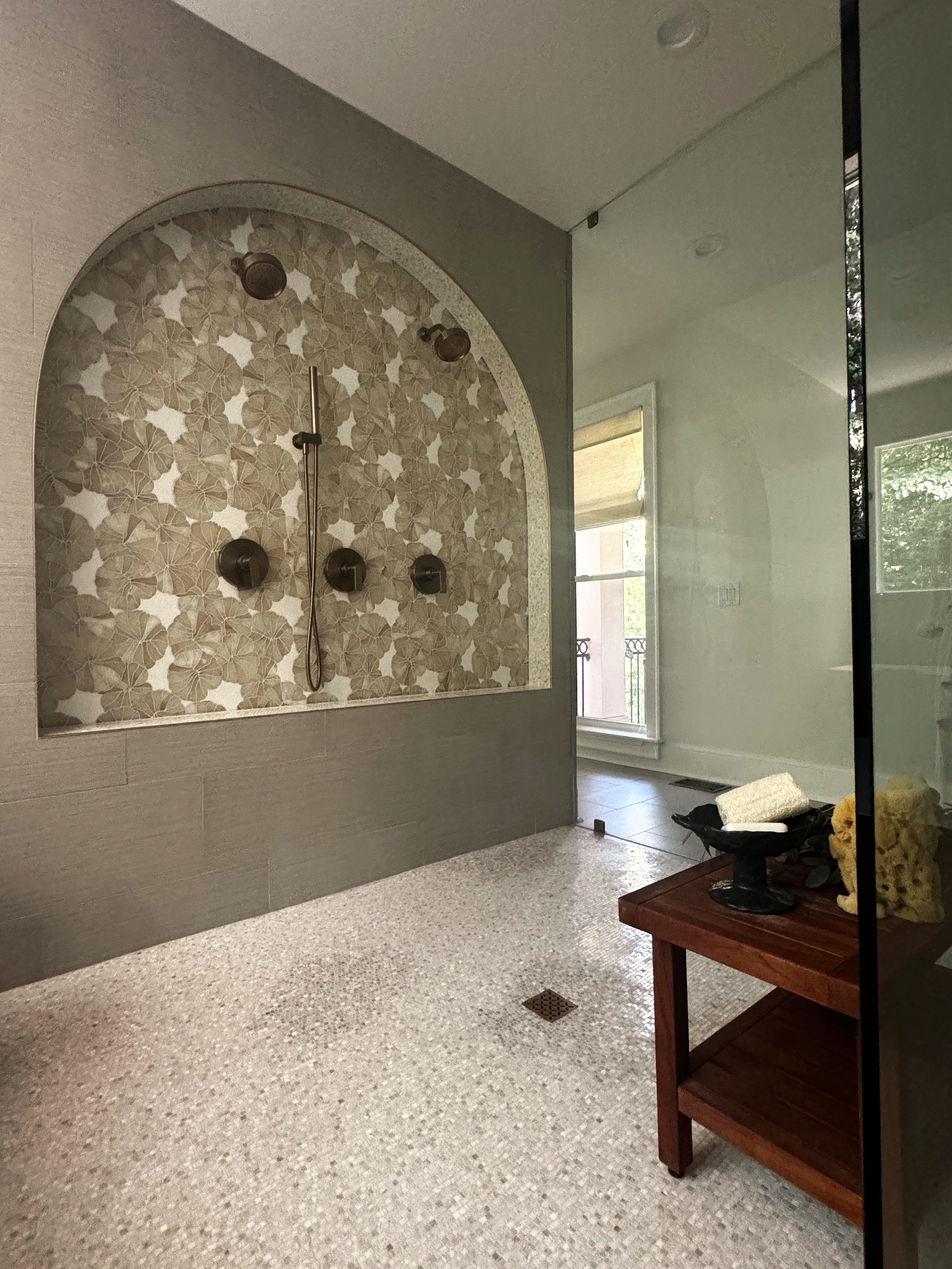 Arched shower niche with floral mosaic tile and dual shower heads.