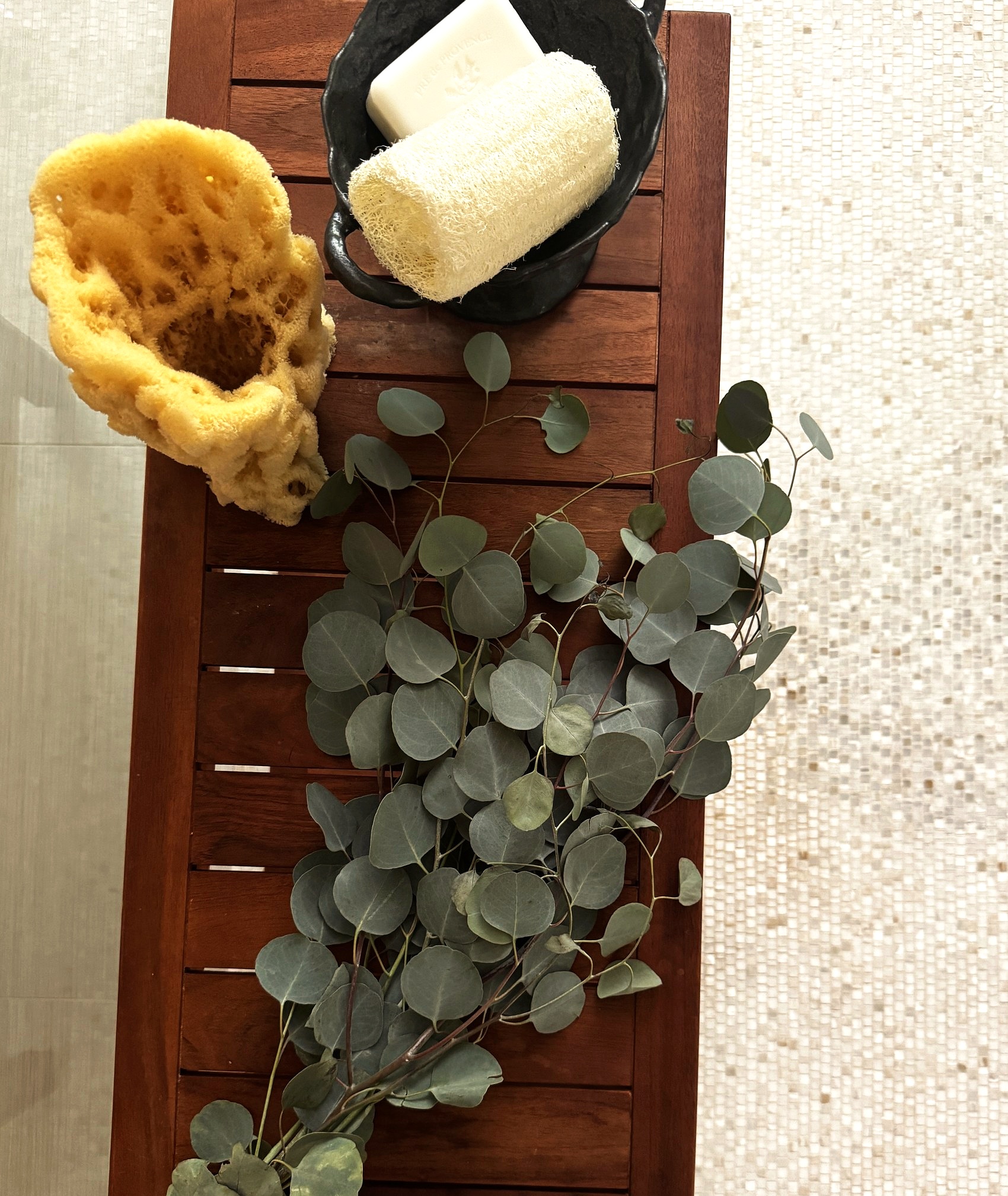 Flat lay of natural sponges, soap, and eucalyptus on a teak bench.