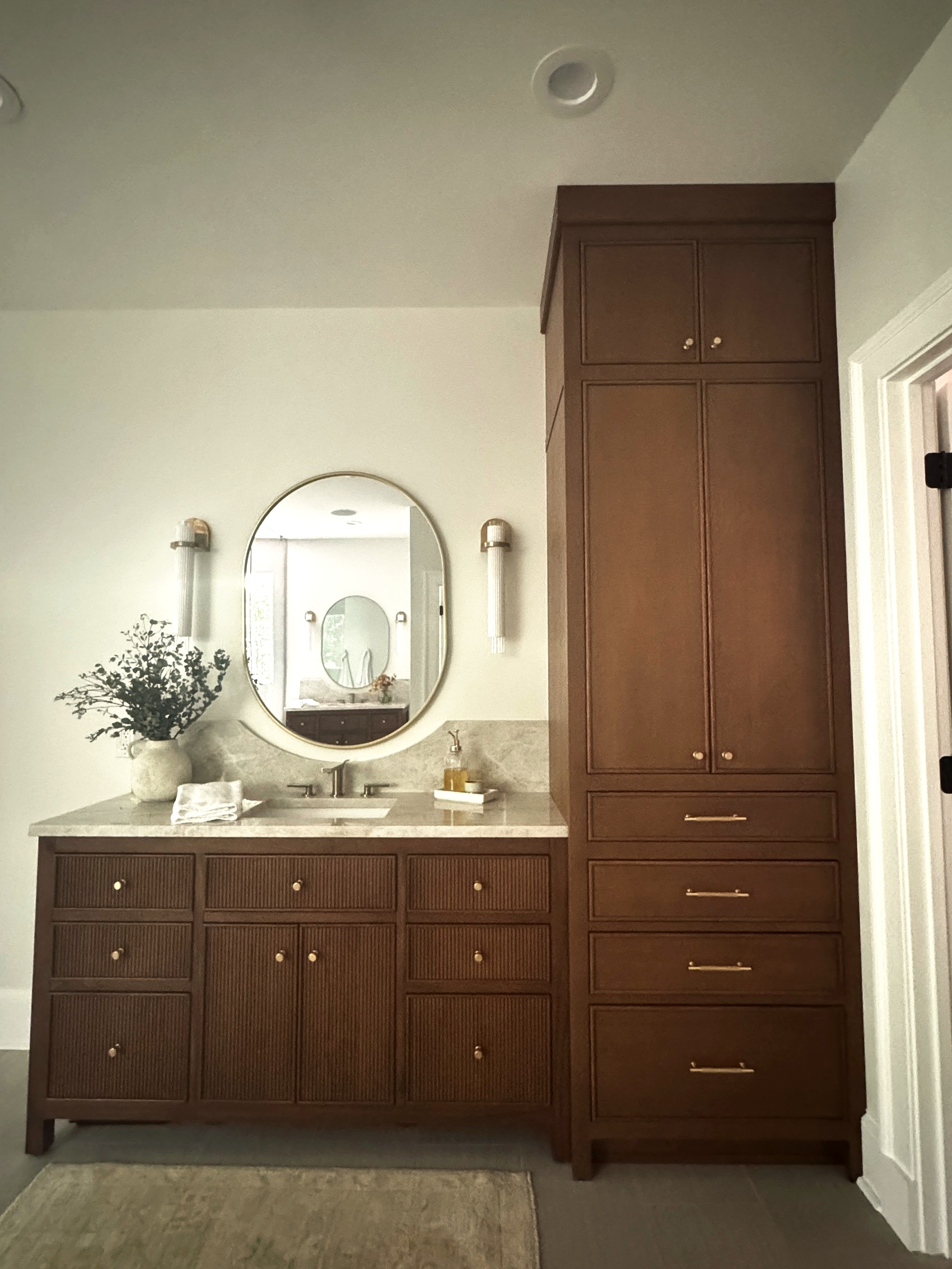 Wide view of dark wood vanity with tall linen cabinet.