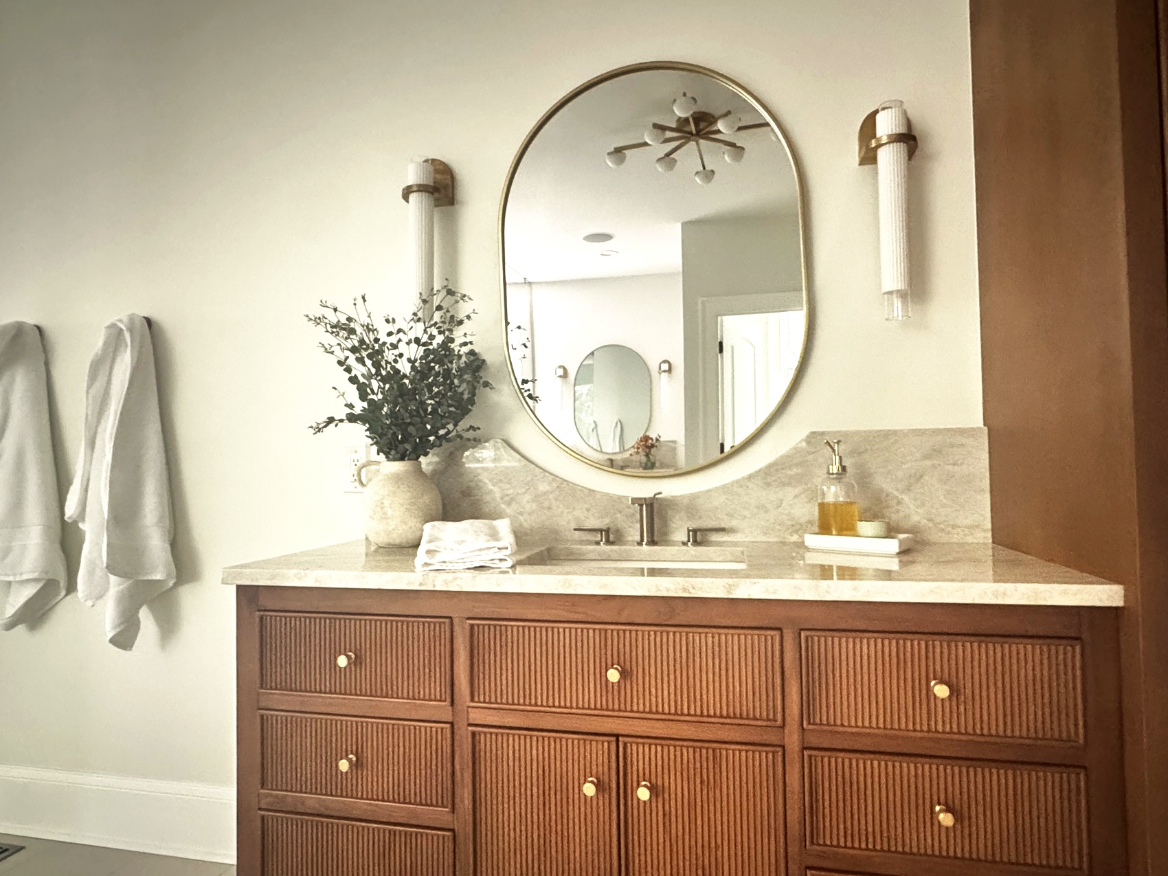 A styled walnut bathroom vanity with a brass mirror and fresh eucalyptus.