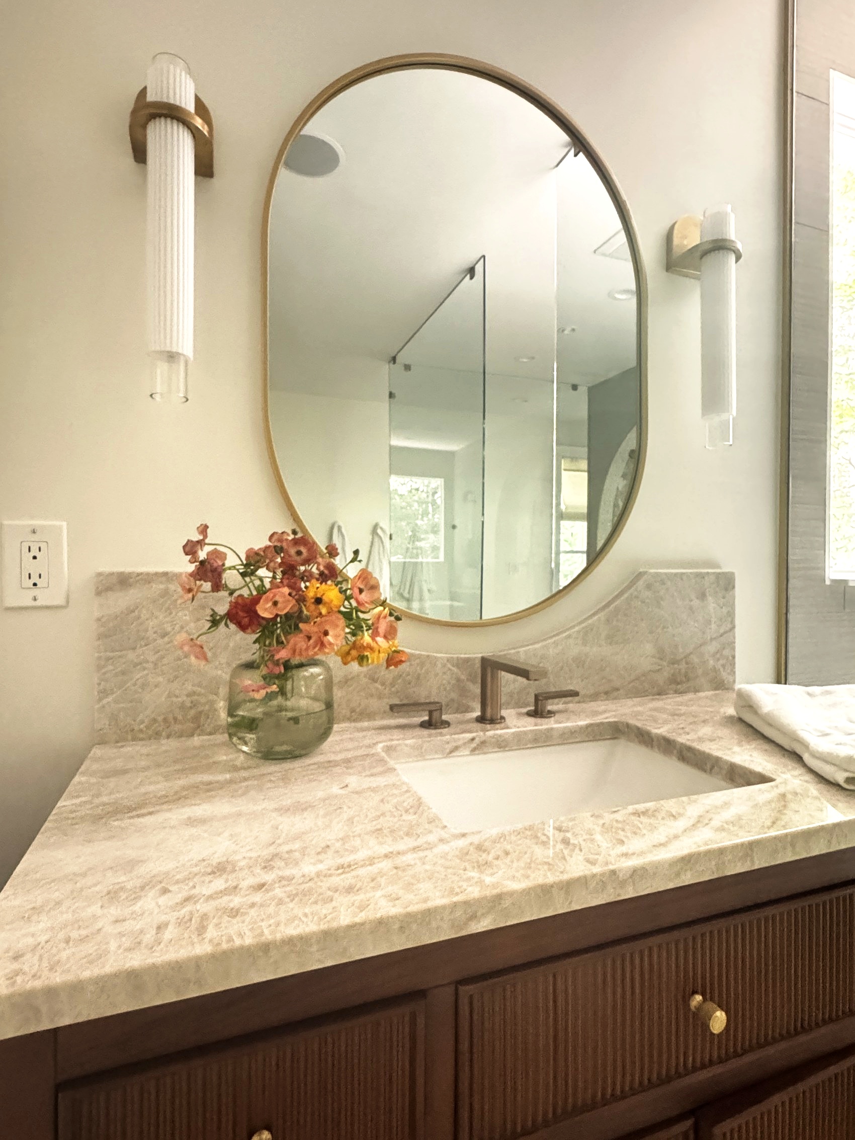 Walnut vanity detail styled with a ceramic vase and fresh flowers.