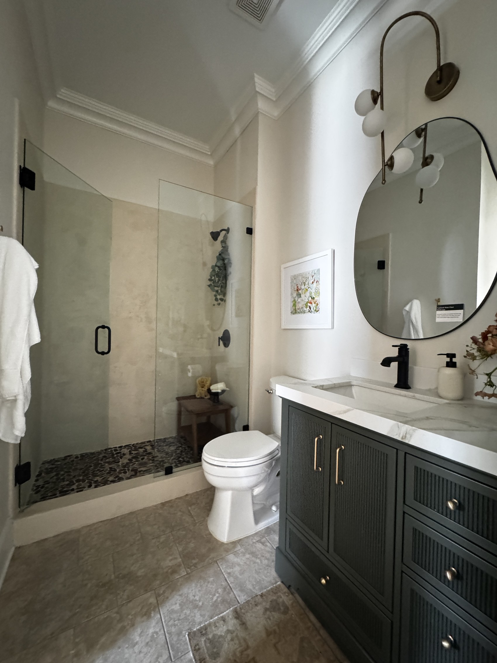 Primary bathroom with glass shower, dark vanity, and round mirror.