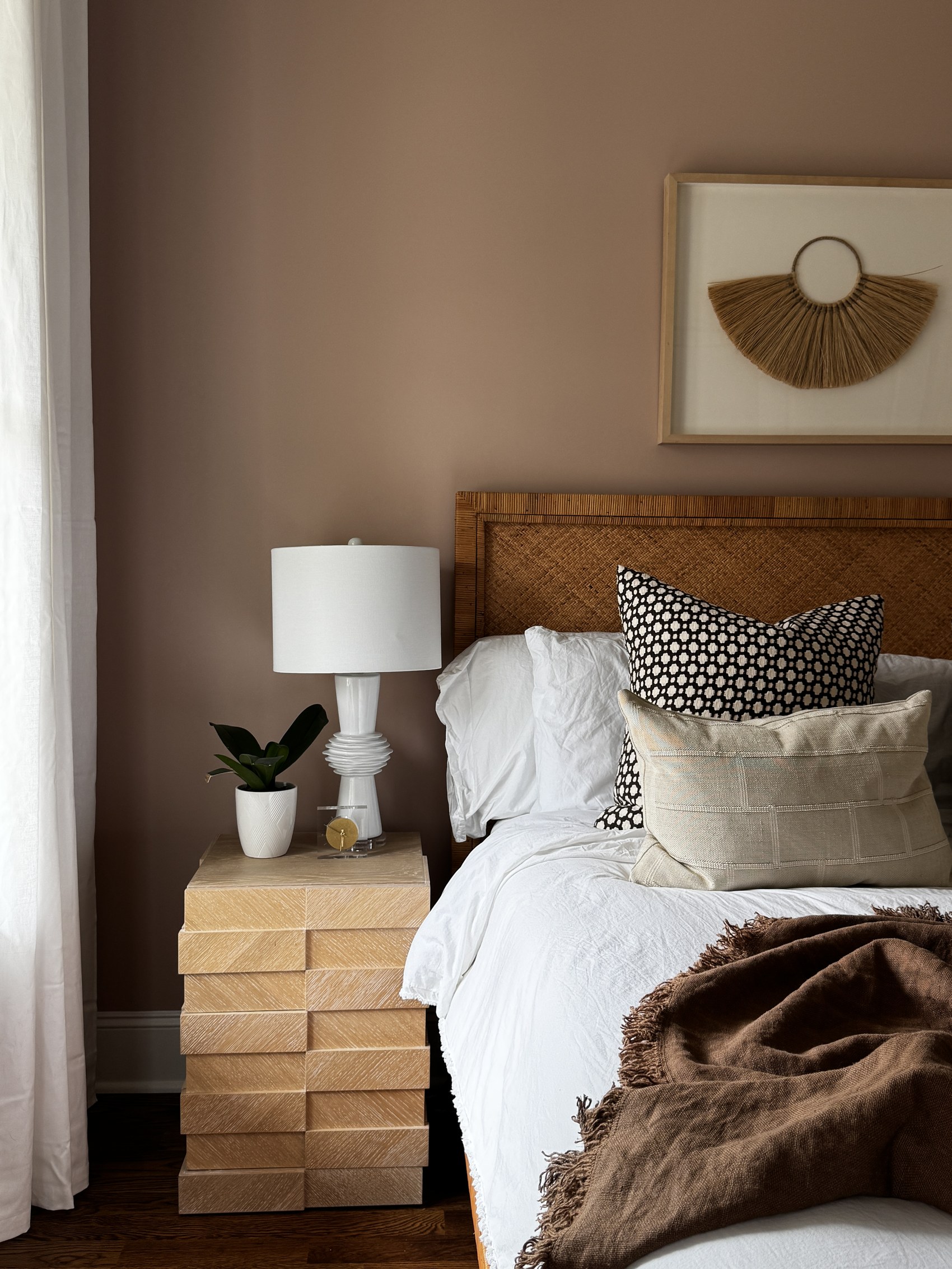 Primary bedroom with rattan headboard, mauve walls, and patterned pillows.