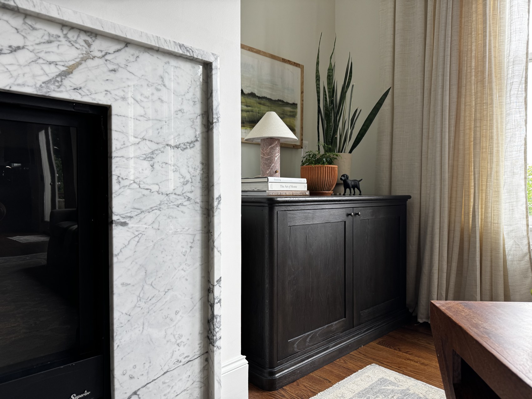 Marble fireplace surround beside a dark cabinet styled with books and a plant.