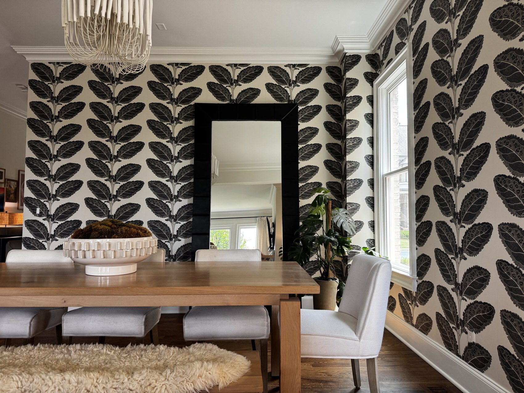 Dining room with bold black and white botanical wallpaper, wood table, and sheepskin rug.