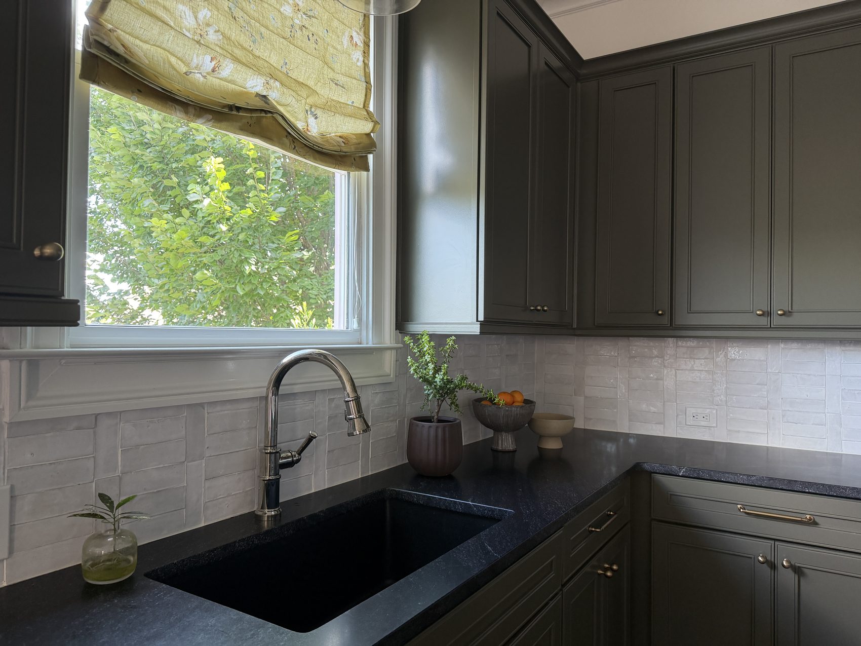 Kitchen sink beneath a window with a floral roman shade and zellige tile backsplash.