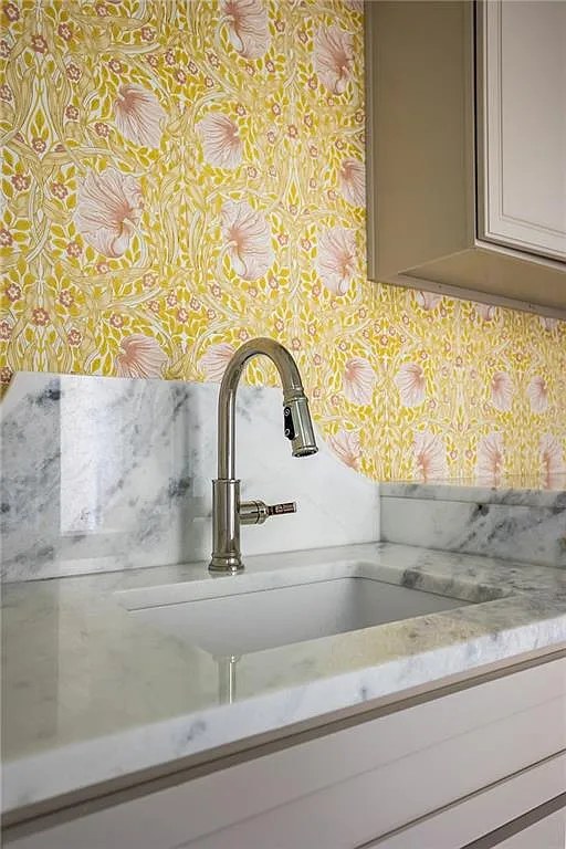 Detail of laundry sink faucet against yellow and pink floral wallpaper.