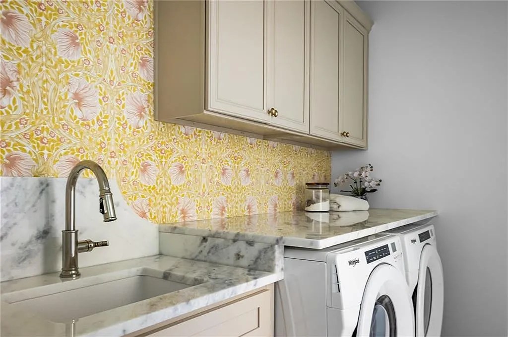 Laundry room sink with marble counter and yellow botanical wallpaper.