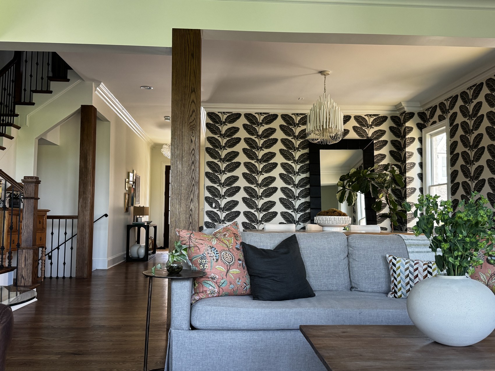 Living room with black and white botanical wallpaper, black-framed mirror, and gray sofa.