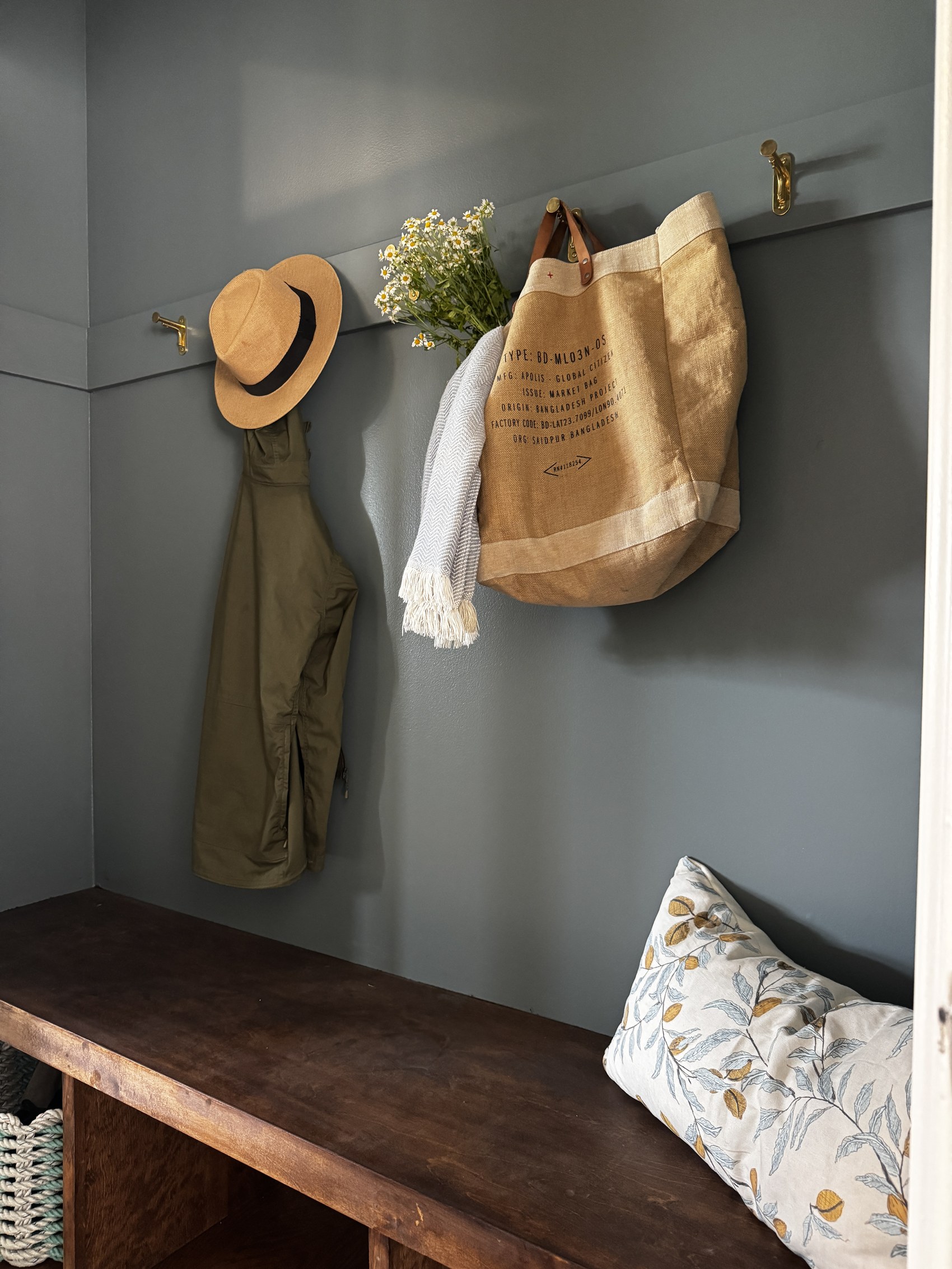 Mudroom nook with brass hooks, a sun hat, tote bag, and wildflowers.