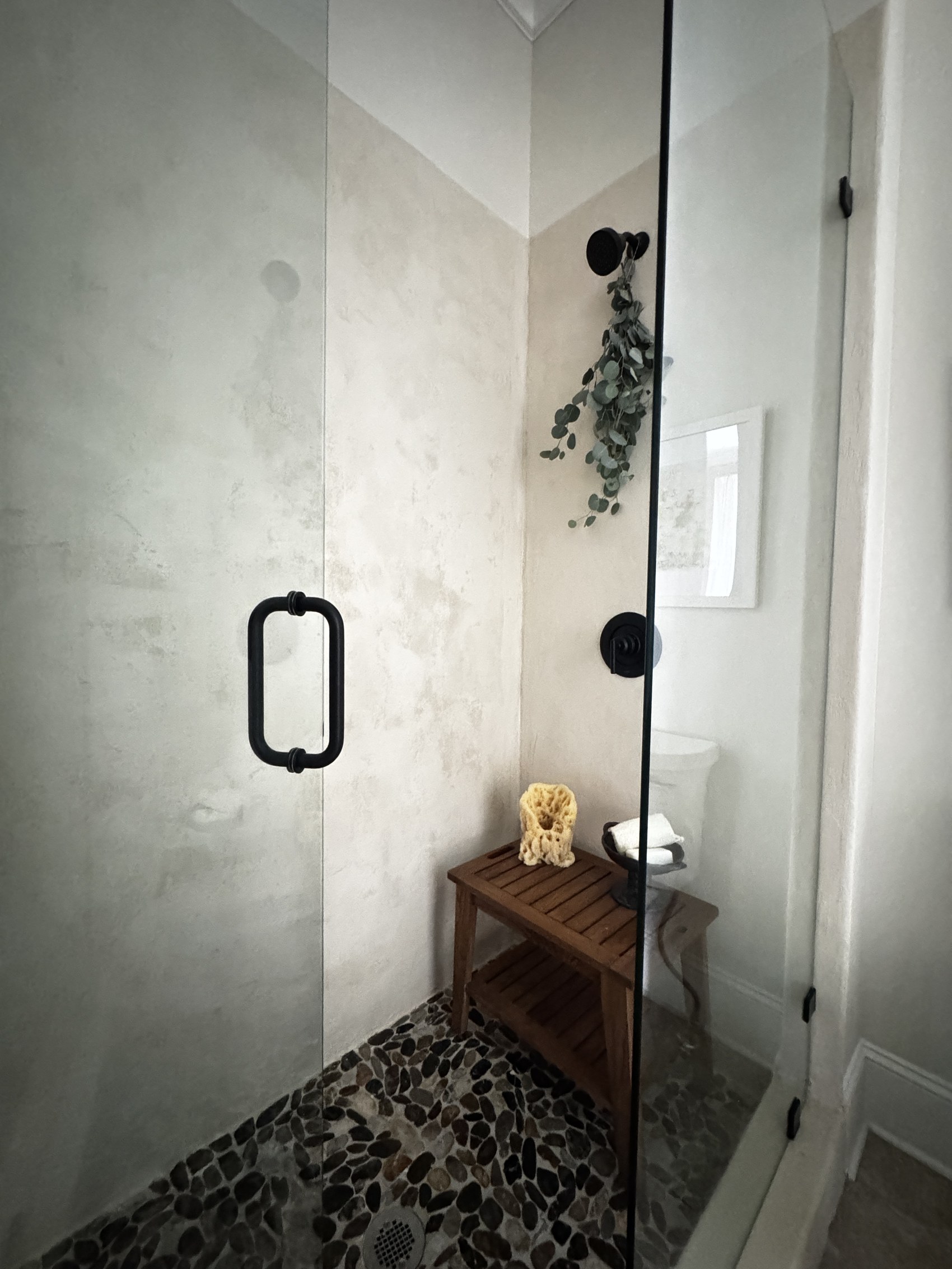 Spa-style shower with pebble floor, teak stool, and hanging eucalyptus.