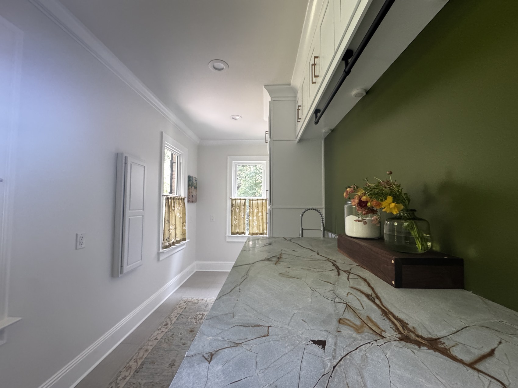 Laundry room with olive green accent wall, marble waterfall counter, and cafe curtains.