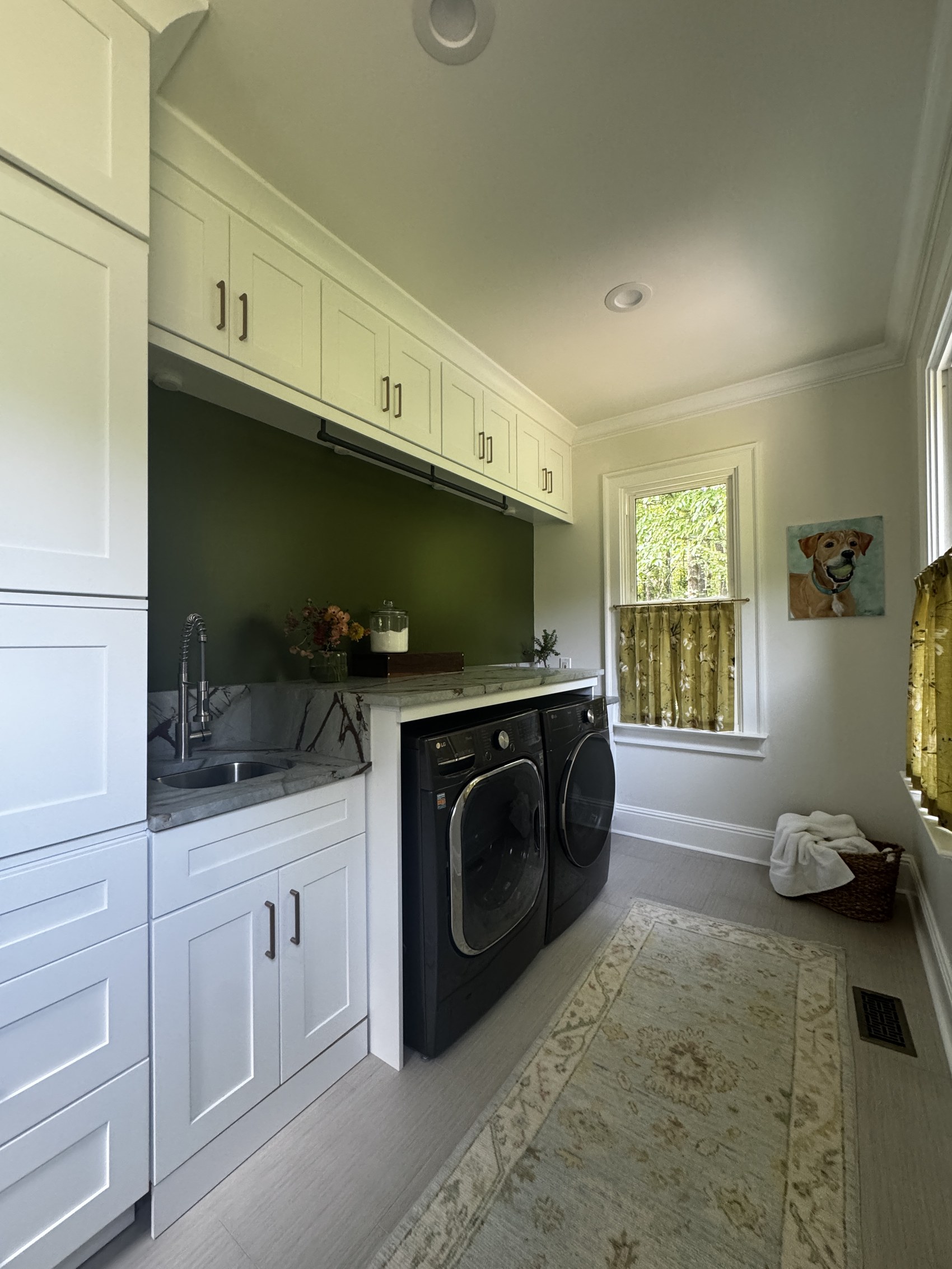 Wide view of laundry room with runner rug and pet portrait.