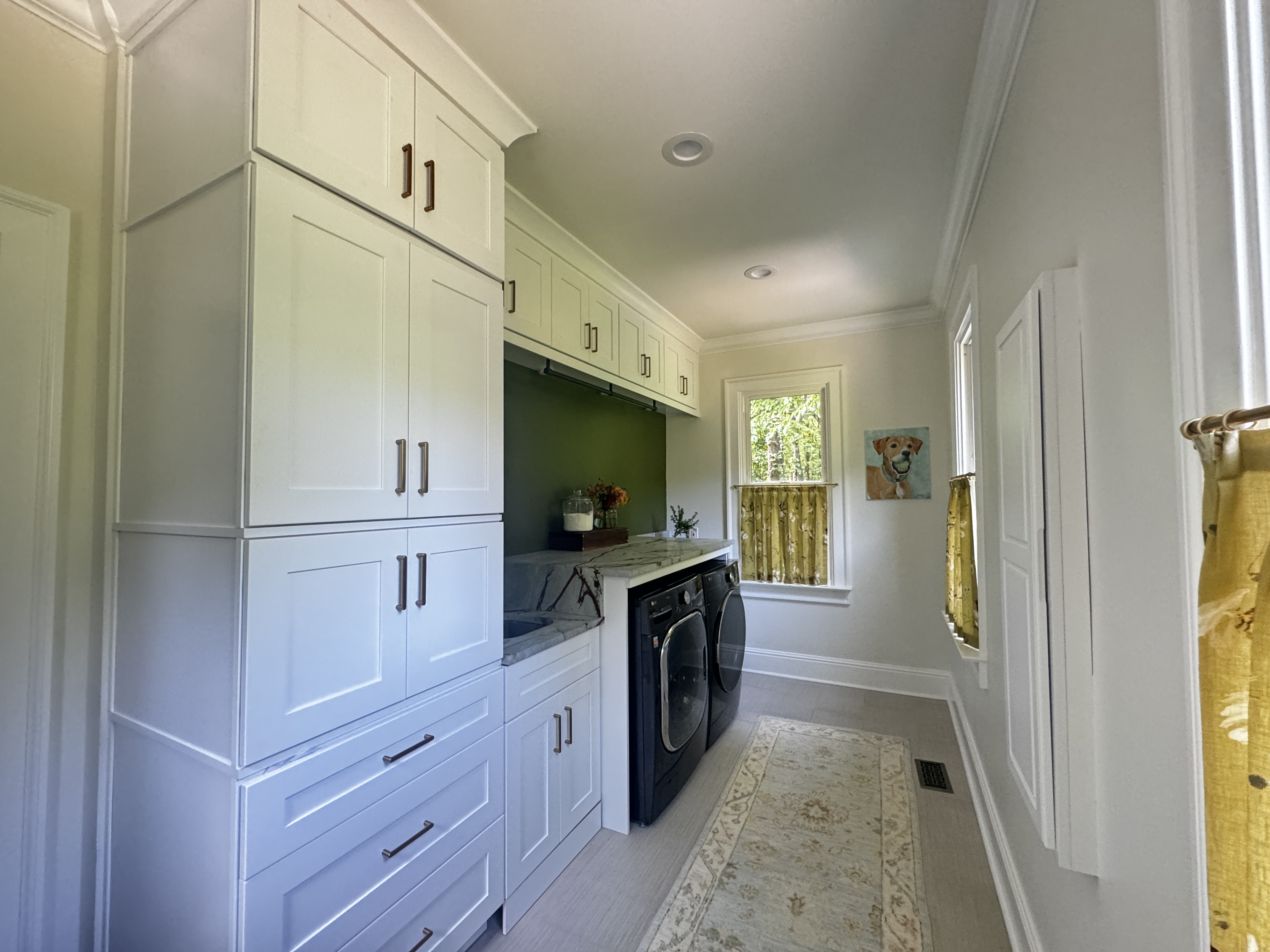 Laundry room view showing full upper cabinetry, olive accent wall, and washer and dryer.