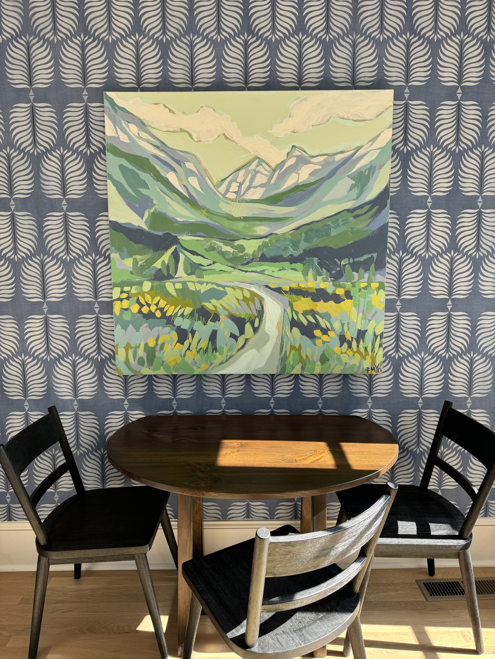 Original landscape painting hung above a breakfast nook with patterned wallpaper.