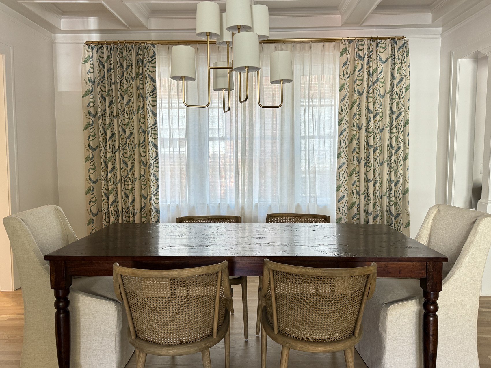 Dining room with cane-back chairs, botanical curtain fabric, and a drum-shade brass chandelier.