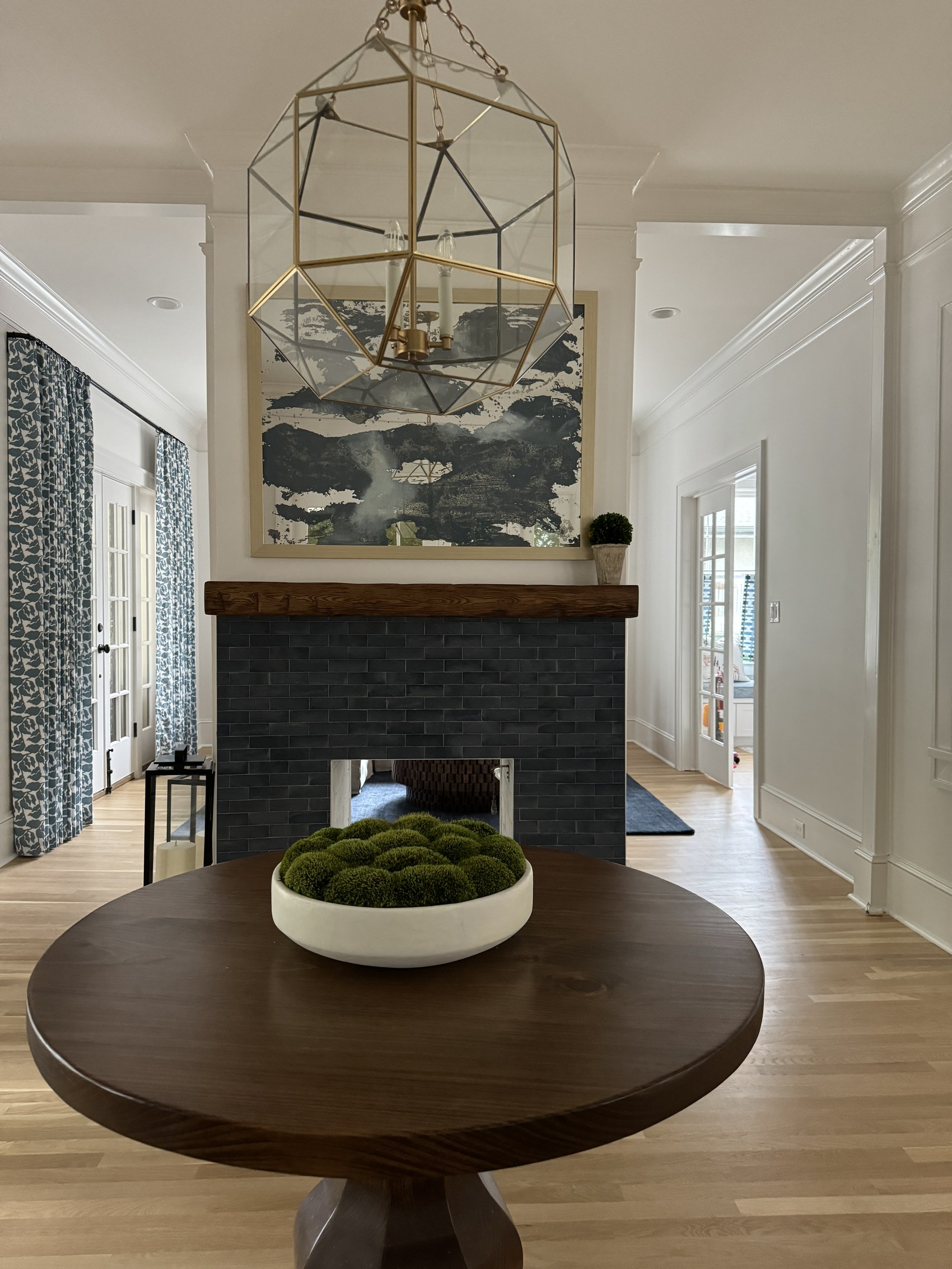 Entry with round wood table, moss bowl centerpiece, black tile fireplace, and geometric brass pendant.