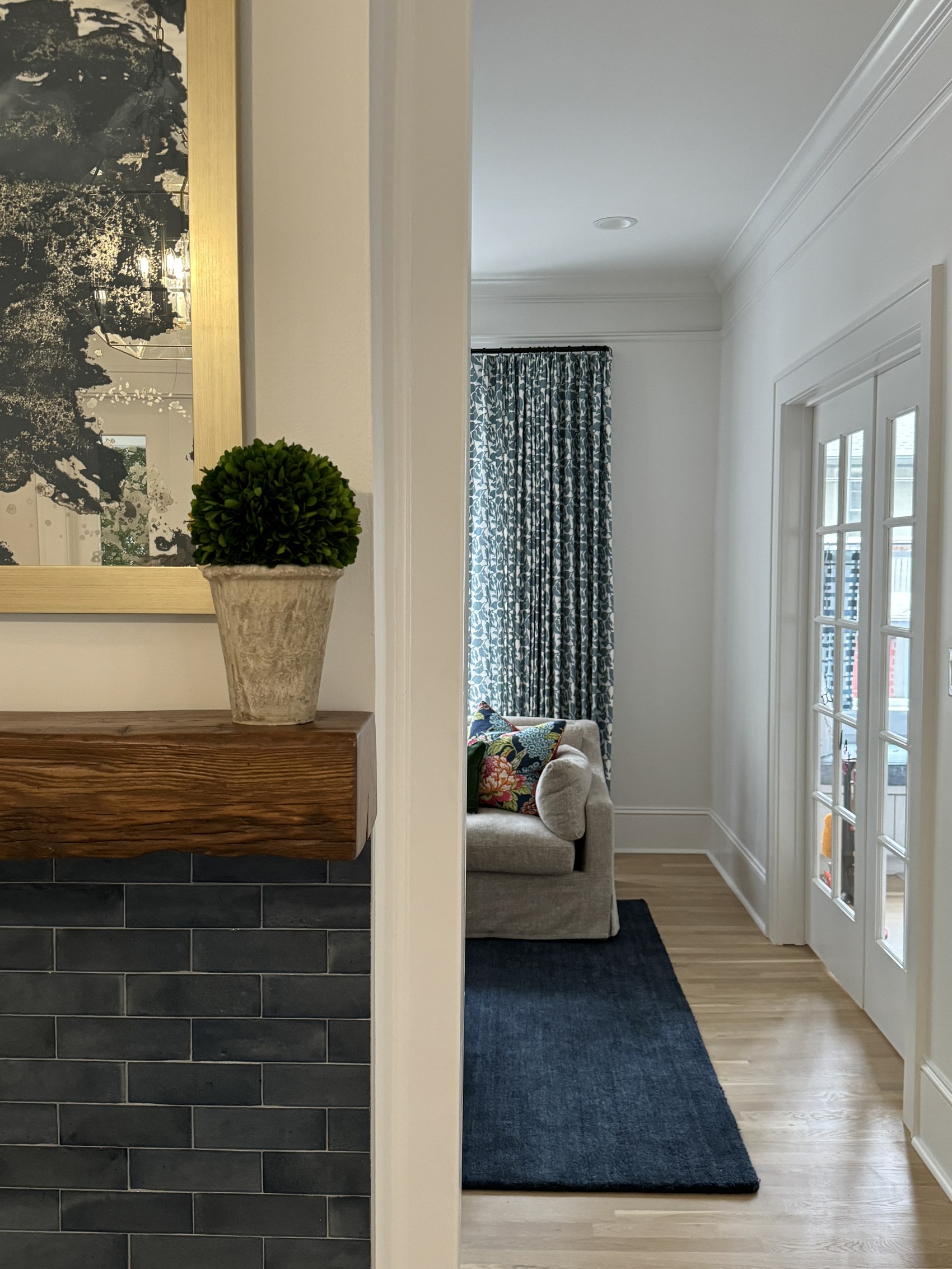 View through the entry toward a sitting room with floral curtains and a navy rug.