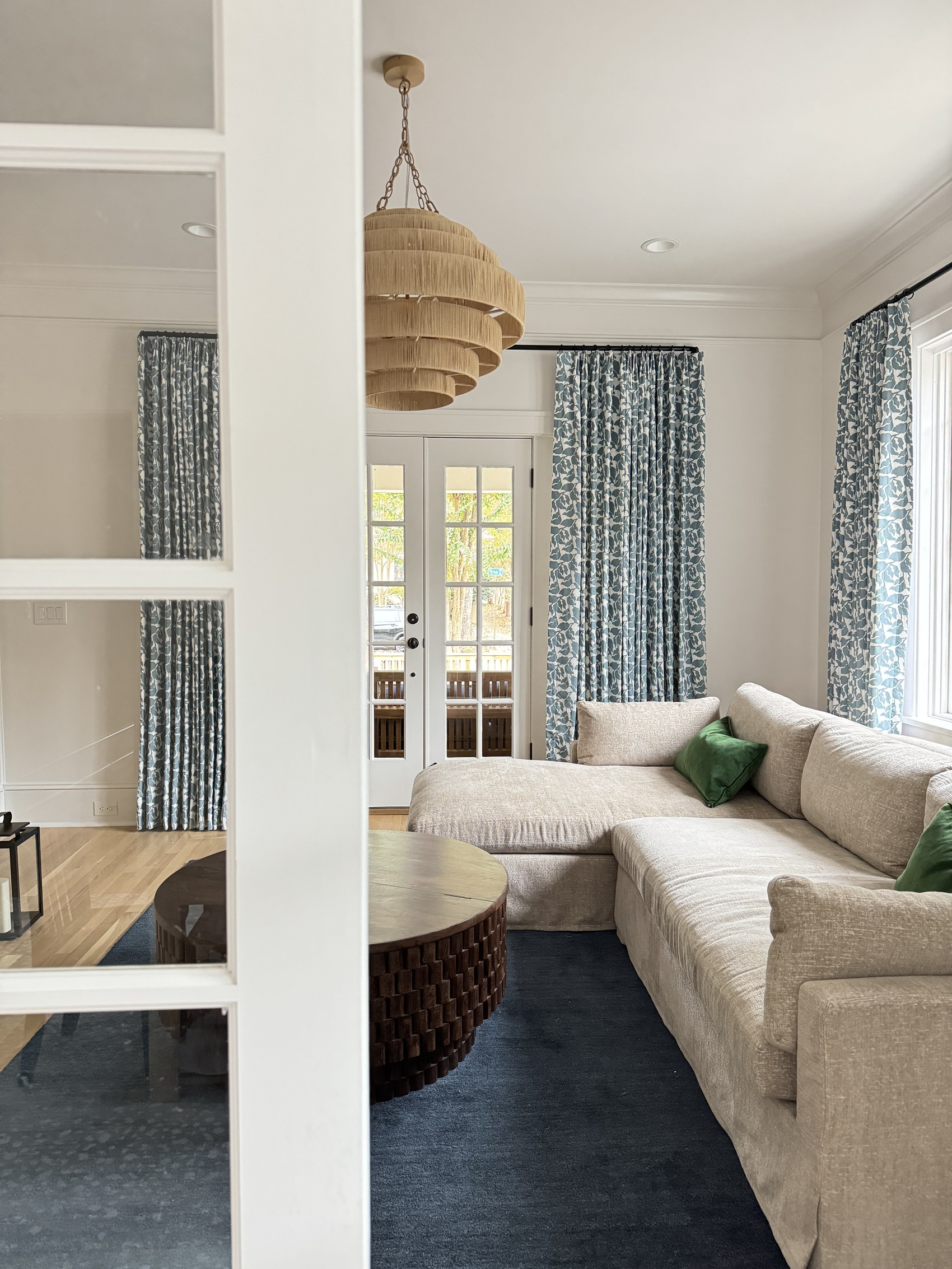 Living room sectional viewed through a doorway with blue floral curtains.