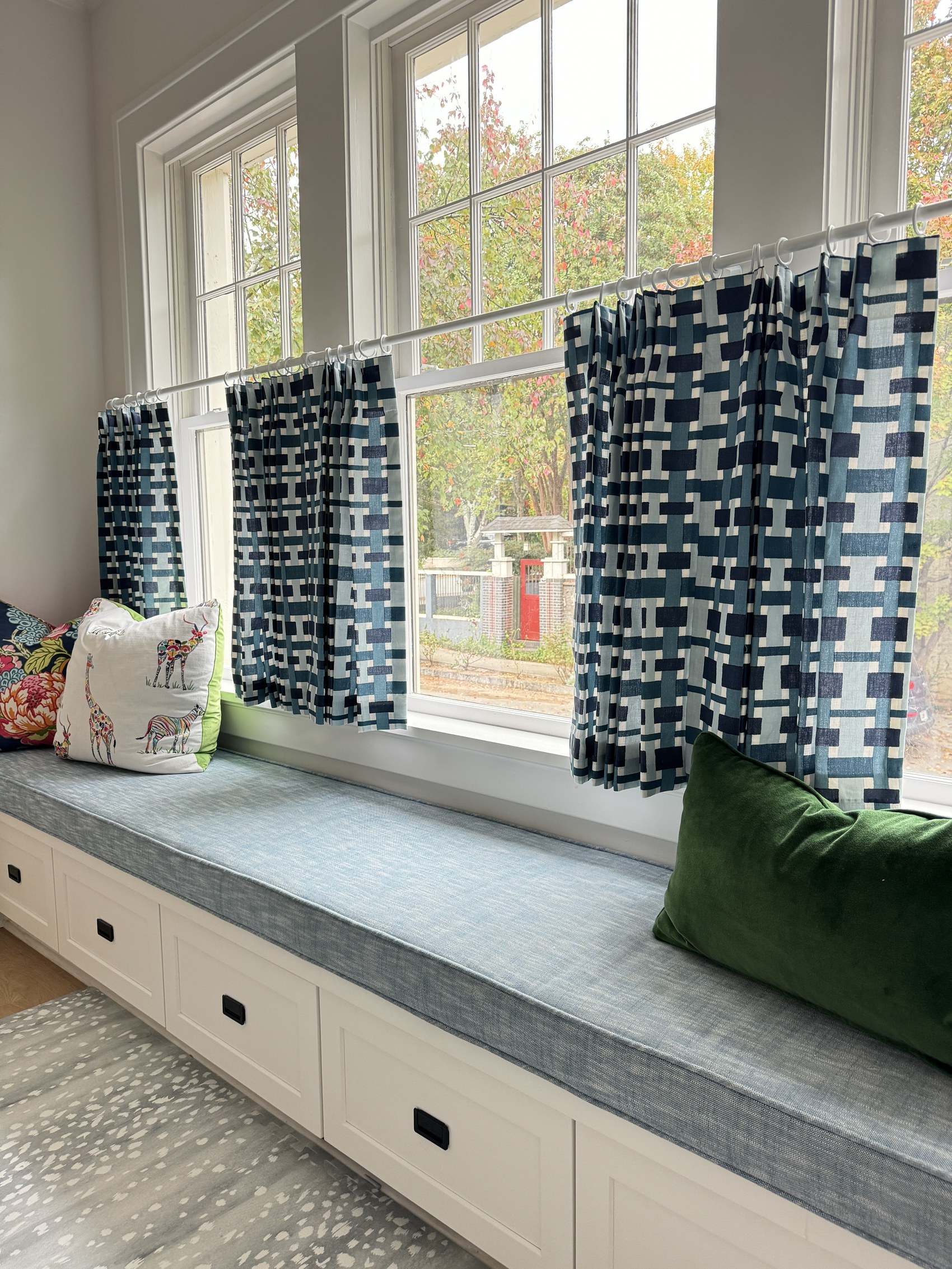 Window seat styled with patterned cushions and a giraffe-print pillow beneath blue geometric curtains.