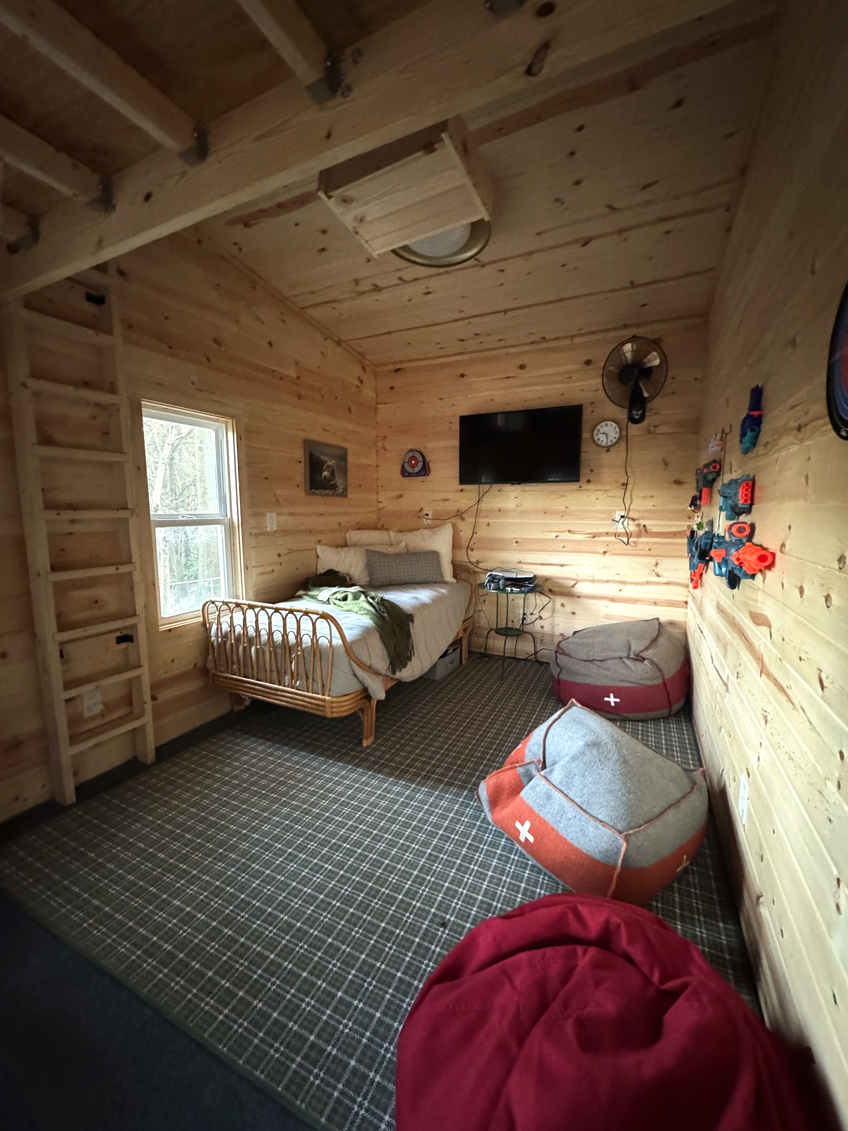 Wood-paneled bunkhouse bedroom with a rattan bed, TV, and plaid carpet.