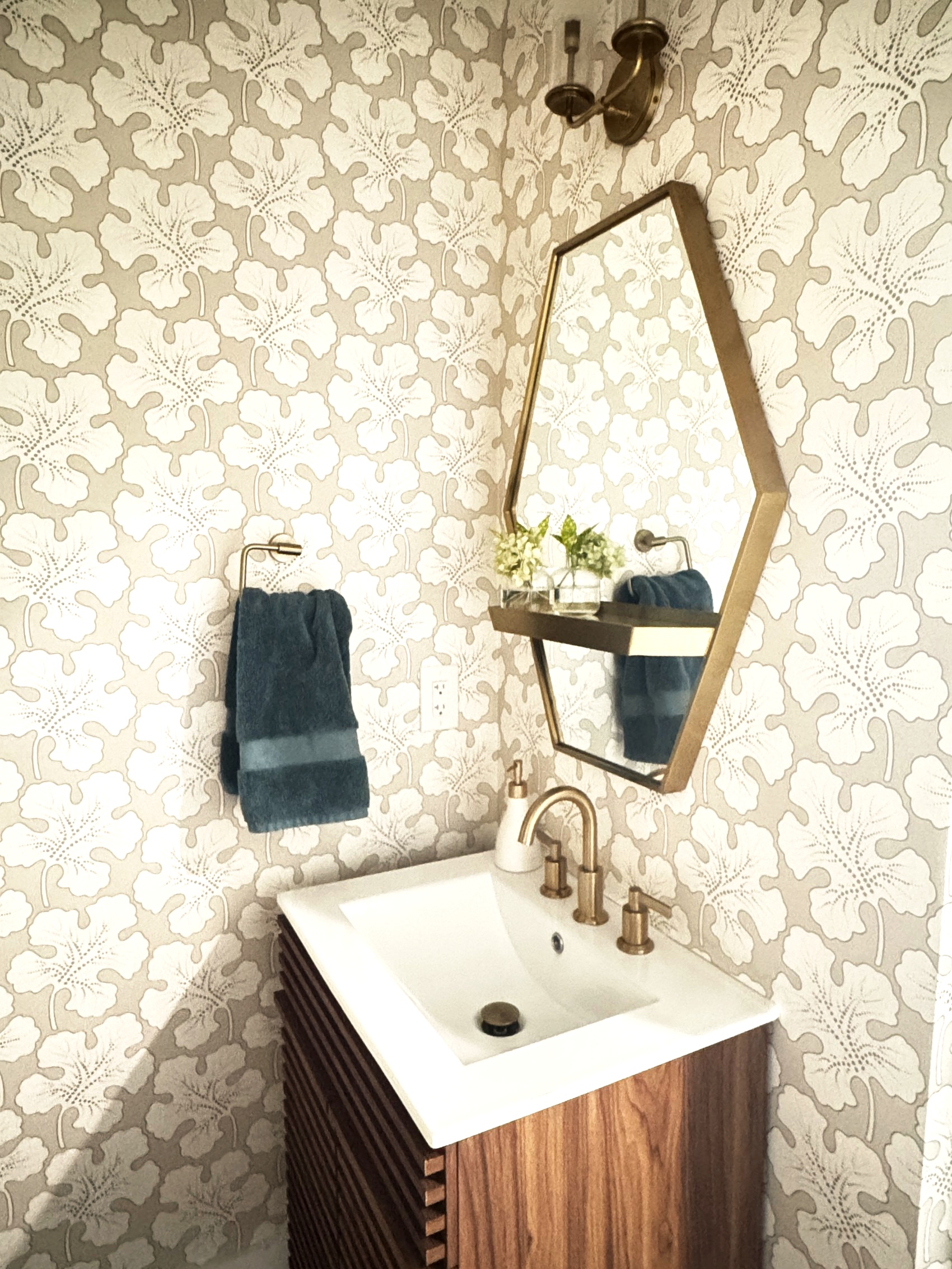 Powder room with botanical wallpaper and a hexagonal brass mirror.