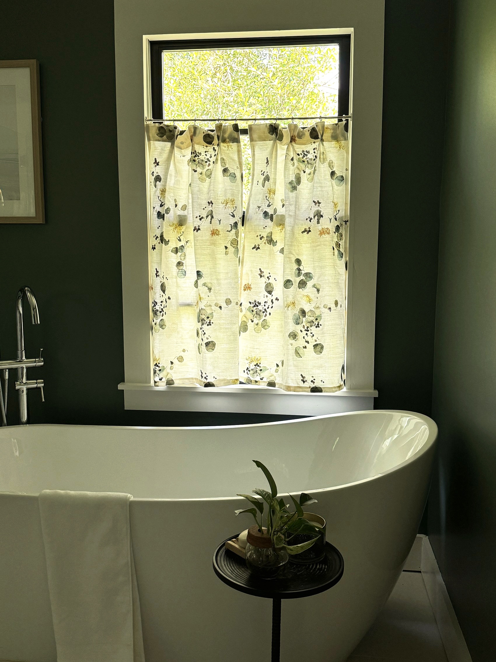 Freestanding soaking tub beneath a botanical cafe curtain.