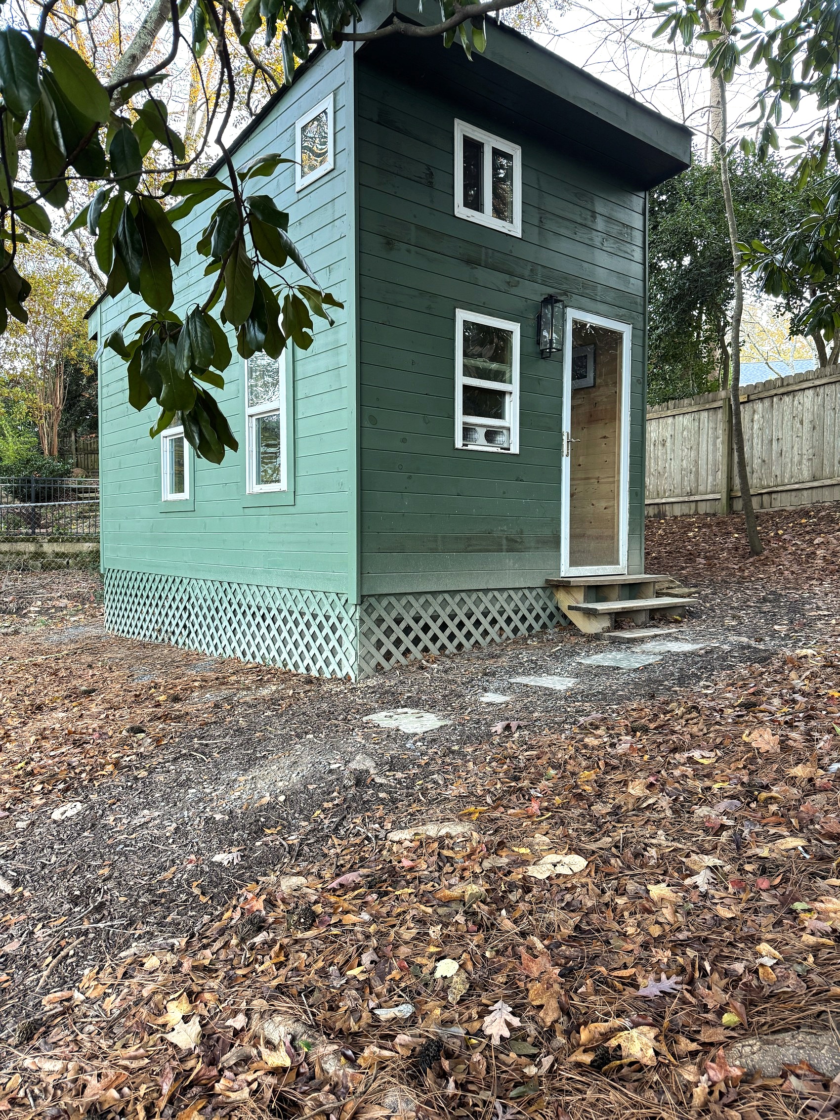 Exterior of a small green backyard outbuilding surrounded by trees.