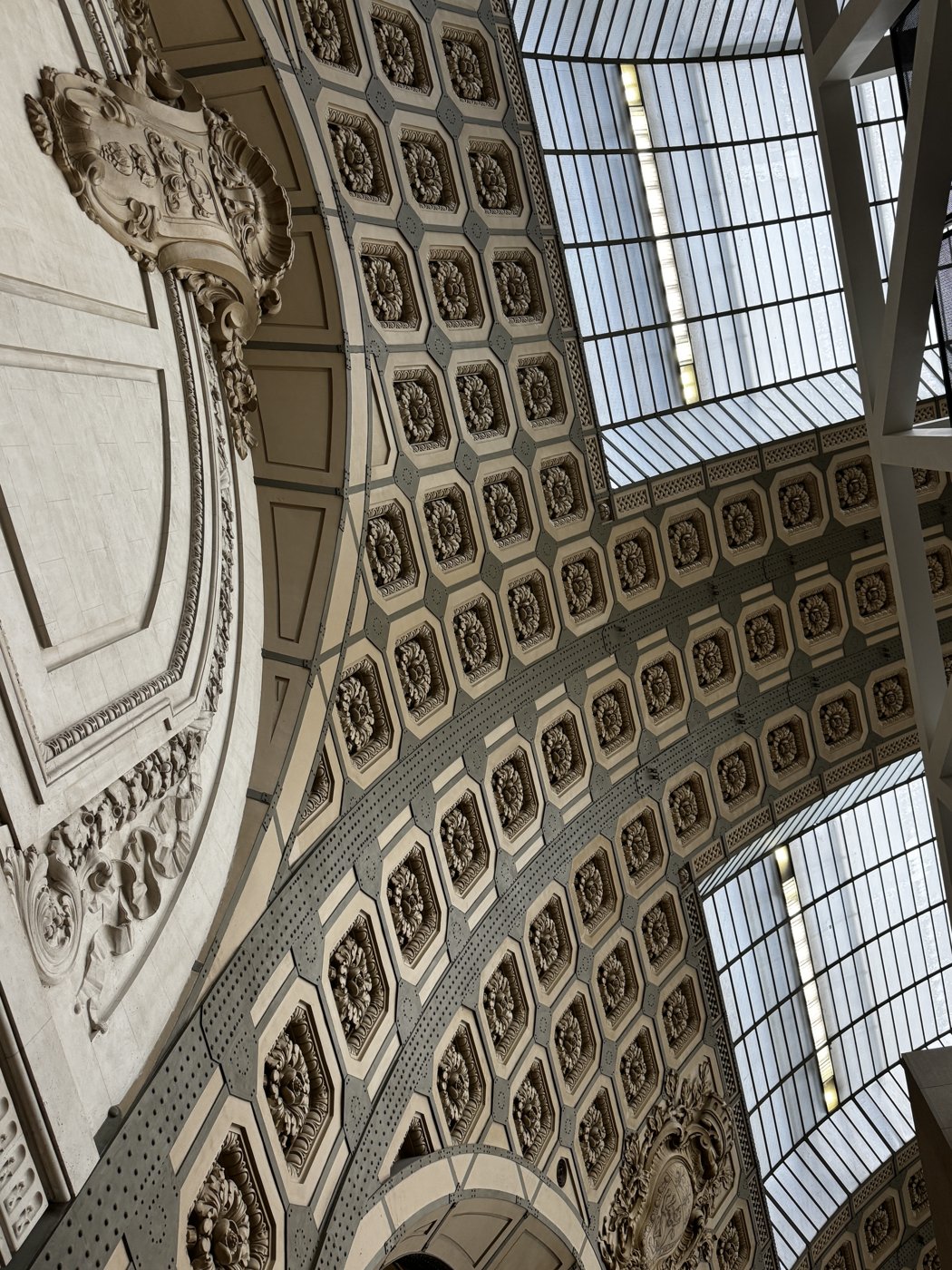 An ornate coffered ceiling with carved rosettes, seen from below a museum atrium.